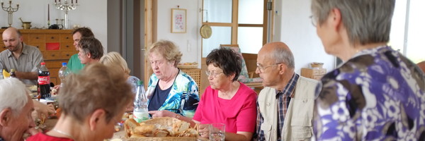 Viele - vor allem ältere - Menschen sitzen um einen Tisch und essen gemeinsam